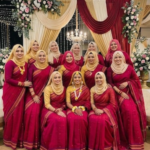 May include: A group of thirteen individuals wearing matching magenta sarees with gold borders and gold hijabs. The sarees feature subtle gold patterns, and some individuals wear yellow and white floral garlands around their necks or wrists.