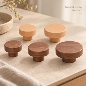 Puede incluir: Una colección de cinco pomos redondos de madera para armarios en varios tamaños y dos tonos de madera, claro y oscuro. Los pomos presentan una parte superior circular plana y una base cilíndrica. El texto Natural Living Hardware es visible arriba a la derecha.