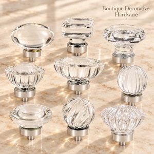 May include: A collection of nine clear glass cabinet knobs with silver-toned metal bases, featuring various shapes including round, square, fluted, and ribbed designs. The text Boutique Decorative Hardware is visible in the upper right corner.
