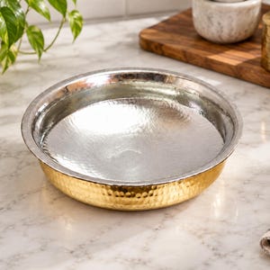 May include: A round, shallow bowl featuring a hammered texture. The exterior of the bowl has a bright gold-tone finish, while the interior surface is finished in a contrasting silver-tone metal. The bowl has a smooth, rounded rim.