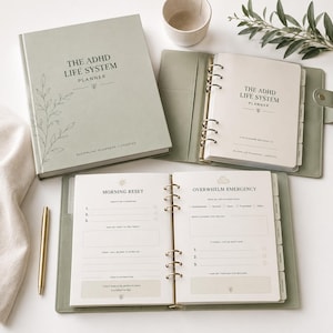 May include: A sage green planner set titled The ADHD Life System Planner, featuring a hardcover book, a six-ring binder with internal pages, a gold pen, and tabbed dividers. The open pages display sections for Morning Reset and Overwhelm Emergency.