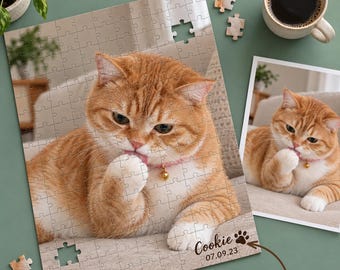 May include: A custom jigsaw puzzle featuring a ginger cat wearing a pink collar with a bell, licking its paw. The puzzle includes the printed text Cookie and the date 07.09.23, accompanied by a paw print icon and a reference photo.