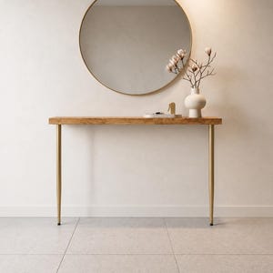 May include: A rectangular wooden console table with a natural grain finish and two slender, tapered gold metal legs. The table is topped with a white ceramic vase containing flowering branches and a small white tray with gold decorative items.