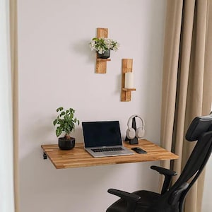 Peut inclure: Un bureau mural en bois avec une finition à grain naturel, comprenant un ordinateur portable, une petite plante en pot et un smartphone. Au-dessus du bureau, deux étagères murales verticales en bois portent une plante en pot et une bougie.