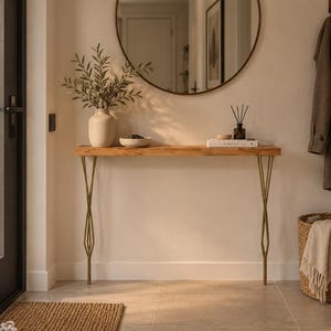 Könnte beinhalten: Ein rechteckiger Holzkonsolentisch mit einer Platte aus Naturholzmaserung und vier schlanken, goldfarbenen Metallbeinen in einem geometrischen, rautenförmigen Design. Der Tisch steht an einer Wand und bietet eine Ablagefläche.