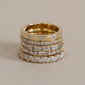 Op de afbeelding: Een stapel van vijf gouden ringen met diverse diamantzettingen, waaronder rond gezette stenen, een pavé-band, een baguette-geslepen band, een gemengde band en een marquise-geslepen eeuwigheidsring. De tekst luidt BHAGWATJEWELLERY.