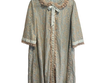 Peut inclure: Une robe en dentelle bleu clair avec un motif floral, bordée de dentelle couleur pêche et d'un col assorti. La robe a un ruban de satin bleu clair et est suspendue à un cintre noir. L'étiquette indique "Yvette Barba Designs."