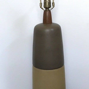 May include: A ceramic table lamp with a brown, beige, and dark gray base. The lamp has a brass harp and a brown wooden finial.