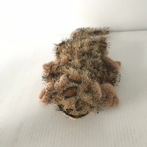 May include: A brown and black plush toy cat with a spotted pattern. The cat is lying on its side with its head turned to the side.