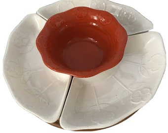 Peut inclure: Un plat de service en céramique blanche avec quatre bols individuels et un bol central. Le bol central est orange et les quatre bols individuels sont blancs avec un motif floral. Le plat est sur une base en bois.