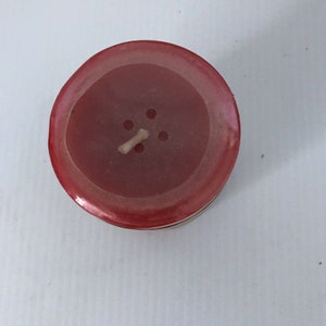 May include: A red candle with a single wick in the center. The candle has a circular shape and a smooth, glossy finish.