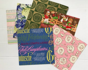 May include: A collection of colorful wrapping paper sheets. Designs include floral patterns, baby-themed illustrations, and birthday greetings in multiple languages. The sheets feature various colors, including blue, pink, green, and brown.