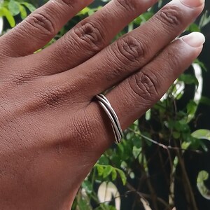 Puede incluir: Un anillo de tono plateado con un diseño de triple banda que consta de tres finos bucles metálicos interconectados que rodean el dedo. El anillo tiene un acabado liso y pulido, con una estructura simple y continua sin piedras ni engastes.