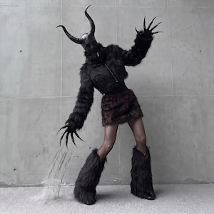 May include: A costume featuring a black faux fur jacket with a zip, a dark brown faux fur skirt, and black faux fur leg warmers. The headpiece is a smooth black mask with two large, curved horns. The hands have long, pointed black claw extensions.