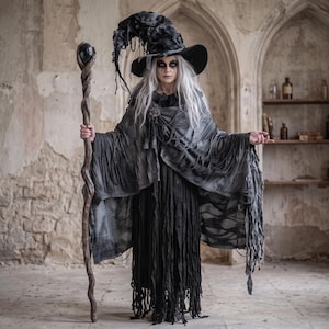 May include: A dark gray and black tattered cloak and dress ensemble featuring a wide-brimmed, distressed pointed hat, long white hair, and a tall, twisted wooden staff topped with a smooth, dark, spherical orb held in a gnarled branch setting.