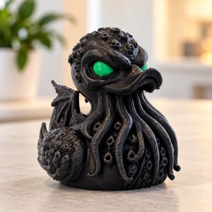 Peut inclure: Une figurine de canard en caoutchouc noir au design inspiré de Cthulhu, avec des tentacules couvrant le visage, de petites ailes sur le dos, une peau texturée et des yeux vert vif. La figurine présente une finition mate et sculptée.