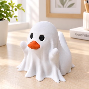 Peut inclure: Une figurine blanche imprimée en 3D en forme de fantôme portant un drap, avec deux yeux noirs ronds et un bec de canard orange proéminent. L'objet présente une surface texturée avec des lignes d'impression horizontales et de petits bras.