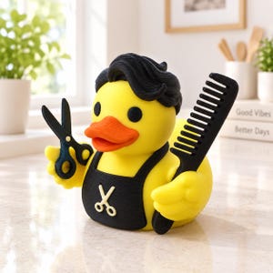 Könnte beinhalten: Eine gelbe Gummiente als Friseur gestaltet, mit schwarzem Haar, einer schwarzen Schürze mit weißem Scherensymbol, die eine schwarze Kunststoffschere in einem Flügel und einen schwarzen Haarkamm im anderen Flügel hält, mit orangefarbenem Schnabel.