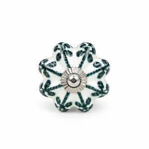 Puede incluir: Un pomo de cerámica blanca para muebles con forma de flor festoneada y un patrón de hojas pintadas en verde oscuro. El centro del pomo tiene una tapa de metal plateado pulido con una pequeña protuberancia redondeada en el punto medio.