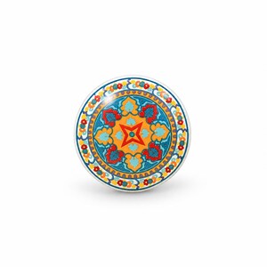 May include: A round ceramic knob featuring a vibrant, multi-colored pattern with a central orange star, surrounded by teal, red, and yellow floral and geometric motifs, finished with a decorative border of small red and yellow circles.
