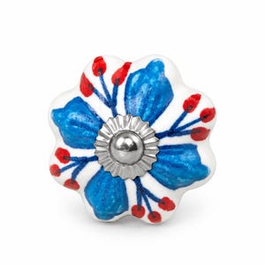 May include: A flower-shaped ceramic cabinet knob with a white base, featuring hand-painted blue petals and small red berries on thin blue stems. A circular, scalloped silver-toned metal hardware piece is centered in the middle of the knob.