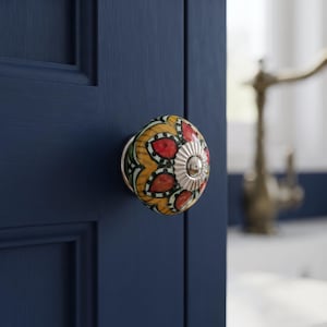 May include: A round ceramic cabinet knob featuring a vibrant floral pattern in shades of red, yellow, and green, accented with black outlines. The center of the knob is finished with a polished silver-tone metal cap and a small central screw.