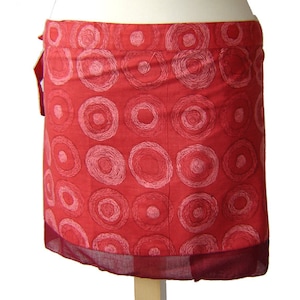 Può includere: Una gonna a portafoglio rossa con un motivo a cerchi bianchi. La gonna ha un bordo bordeaux.