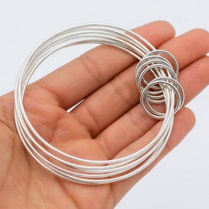 Peut inclure: Un ensemble de plusieurs anneaux métalliques argentés entrelacés. Le design se compose de plusieurs bandes circulaires fines et lisses qui sont reliées entre elles, créant une structure superposée avec une finition métallique polie.