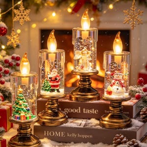 May include: Four cylindrical glass candle lanterns with gold-toned pedestals, each containing a miniature Christmas scene with a Santa, snowman, angel, or tree, topped with a glowing flame-shaped LED bulb and filled with swirling glitter.