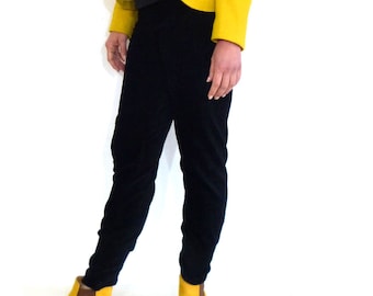 Puede incluir: Una mujer con un blazer amarillo con botones dorados sobre una blusa negra y pantalones negros. Lleva botines amarillos.