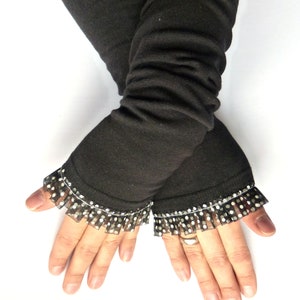 Puede incluir: Calentadores de brazos negros con un borde de encaje de lunares negros y blancos. Los calentadores de brazos están hechos de una tela suave y elástica.