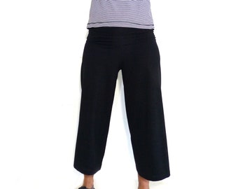 Puede incluir: Una mujer con una camisa de rayas azules y blancas de manga larga y pantalones negros de pierna ancha. Está de pie con las manos en el pelo.