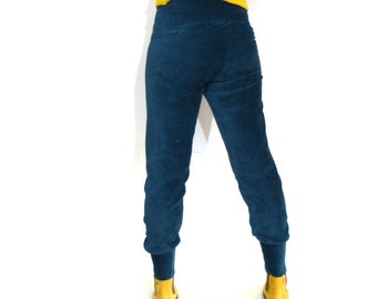 Puede incluir: Una mujer con un suéter amarillo con ribetes de patrón verde y azul y pantalones de pana azul teal.