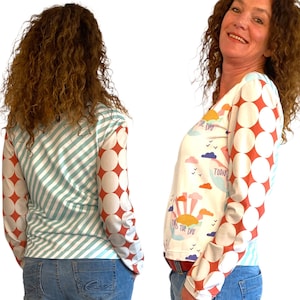 May include: White long-sleeve shirt with a colorful sunrise graphic and the text "It's the day" and "Today is the day". The sleeves have a red and white polka dot pattern.