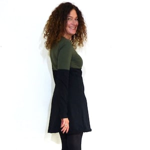 Puede incluir: Una mujer con un vestido negro y verde de manga larga y botas negras. Está de pie frente a un fondo blanco.