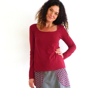 Peut inclure: Une femme portant une chemise à manches longues bordeaux et une jupe grise avec des poches à motifs rouges. Elle porte des collants rouges et des bottes brunes.