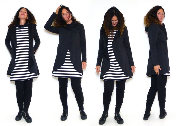 Puede incluir: Una chaqueta negra con capucha y un dise&ntilde;o largo y fluido. La chaqueta se lleva sobre un vestido de rayas blancas y negras. La modelo lleva leggings negros y zapatillas negras.