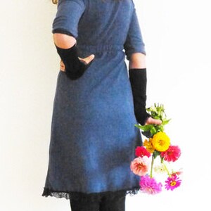 May include: A woman wearing a blue denim dress with black lace trim and black gloves, holding a bouquet of pink, yellow, and orange flowers.