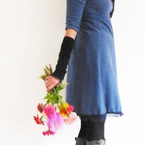 May include: A woman wearing a blue dress with black fingerless gloves and brown boots. She is holding a bouquet of pink, yellow, and orange flowers.