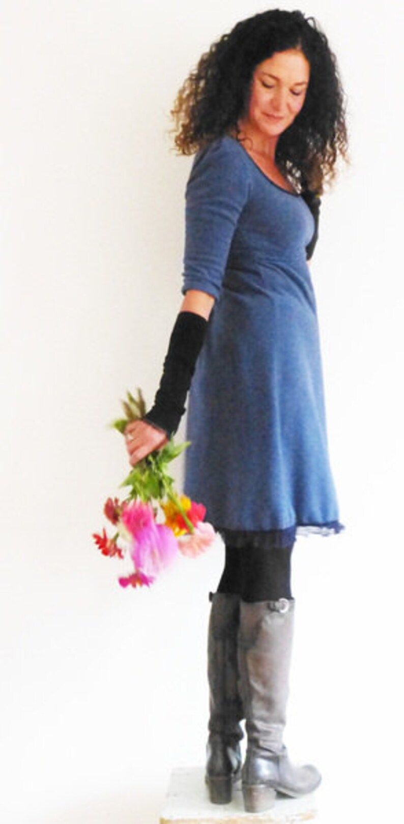 May include: A woman wearing a blue dress with black fingerless gloves and brown boots. She is holding a bouquet of pink, yellow, and orange flowers.