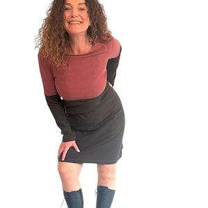 Puede incluir: Una mujer con un vestido de manga larga con la parte superior burdeos y la inferior negra. Lleva botas negras.