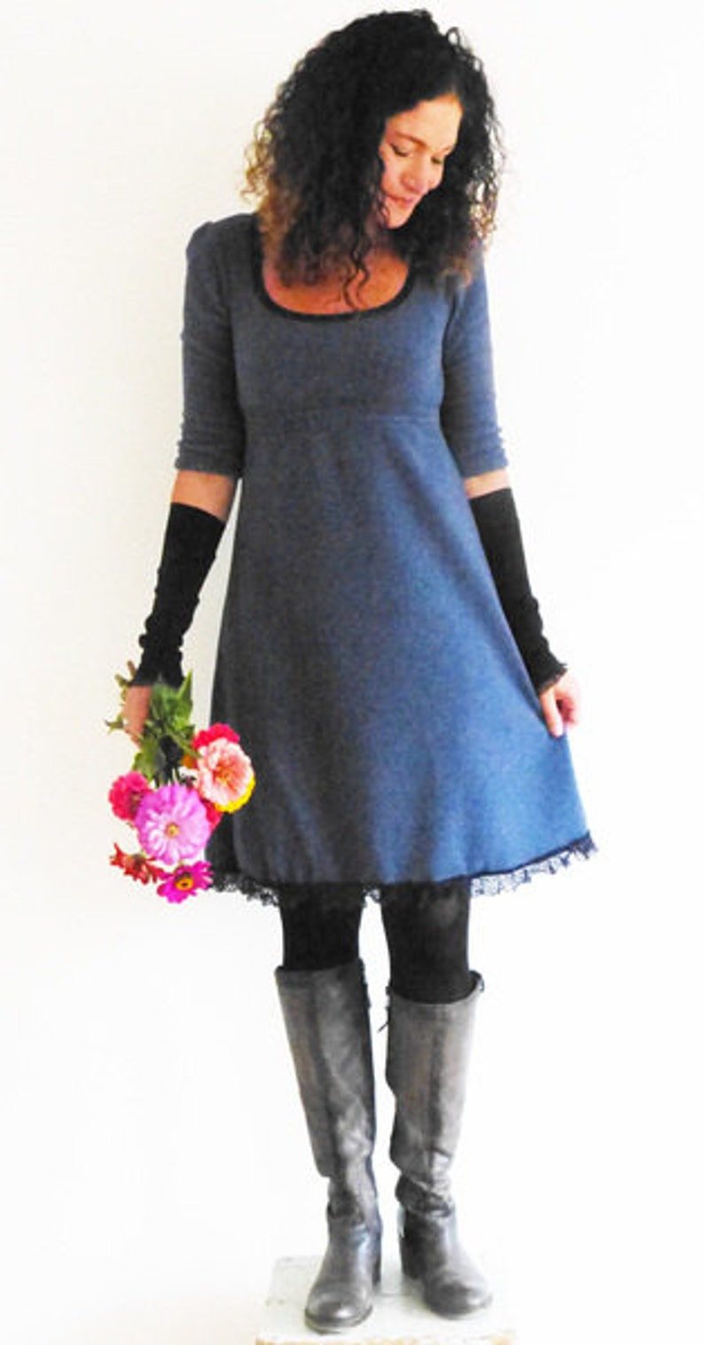 May include: A woman wearing a blue dress with a black lace trim, black fingerless gloves, and black boots. She is holding a bouquet of pink and red flowers.