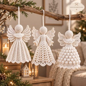 May include: Three off-white crochet angel ornaments hanging from a wooden branch. Each angel features a round head, spread wings, and a unique dress texture: one with vertical pleats, one with a lattice pattern, and one with a bobble stitch design.