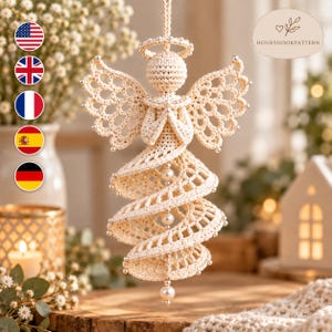 Pode incluir: Um ornamento de anjo em crochê na cor creme com um design intrincado de asas vazadas, uma auréola e uma saia em espiral. A figura é decorada com pequenas contas prateadas nas bordas e um fio vertical de pérolas brancas no centro.