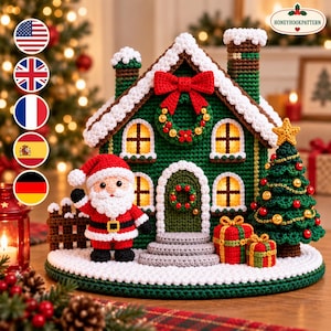 May include: A crochet Christmas scene featuring a green house with white snow-covered roof, a red bow, and a wreath. A Santa Claus figure stands in front, next to a decorated Christmas tree and two wrapped gifts on a circular white base.