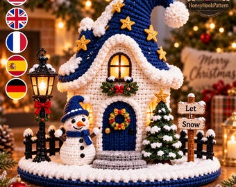 May include: A crocheted winter scene featuring a blue and white house with a lit window, a snowman wearing a blue hat and scarf, a green Christmas tree, a black street lamp, and a sign that reads Let it Snow, all set on a round snowy base.