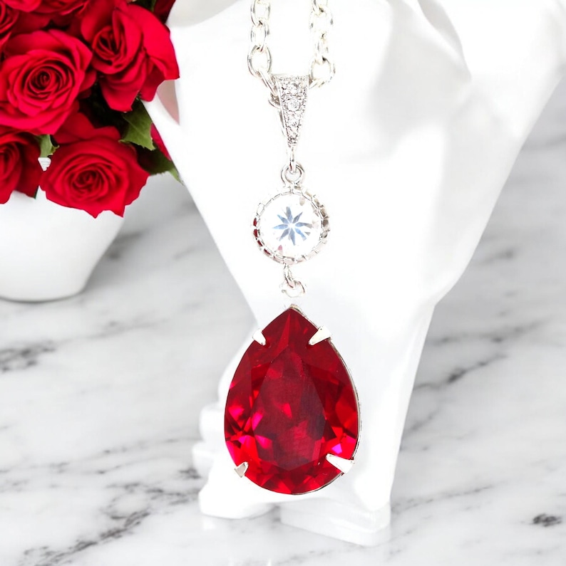 May include: A silver chain necklace with a teardrop-shaped red crystal pendant and a smaller round clear crystal pendant.