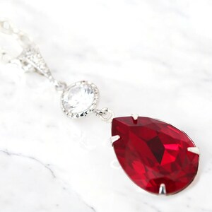 May include: A silver necklace with a clear crystal pendant and a dangling red teardrop-shaped crystal.