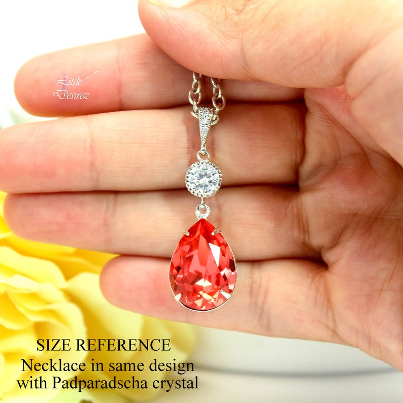May include: A silver necklace with a teardrop-shaped pendant featuring a large, bright orange crystal. The pendant is accented with a smaller, round crystal.
