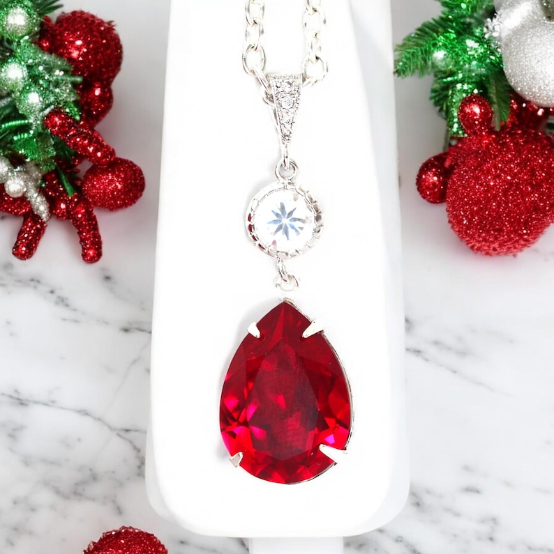 May include: A silver chain necklace with a teardrop-shaped red crystal pendant and a smaller round crystal pendant with a snowflake design.